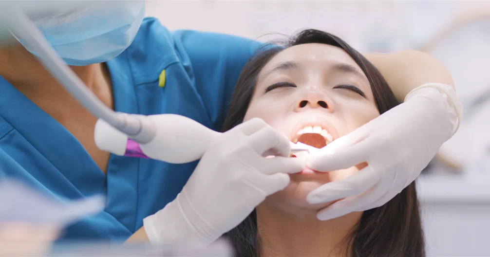 Dentist performing professional gum treatment on female patient in Singapore dental clinic to treat periodontal gum disease.