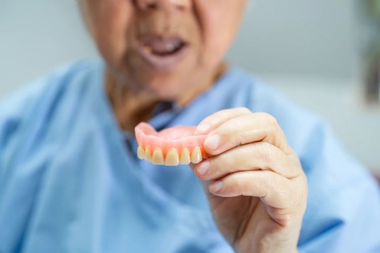An elderly female patients inspect her dentures after removing them for dental procedure.