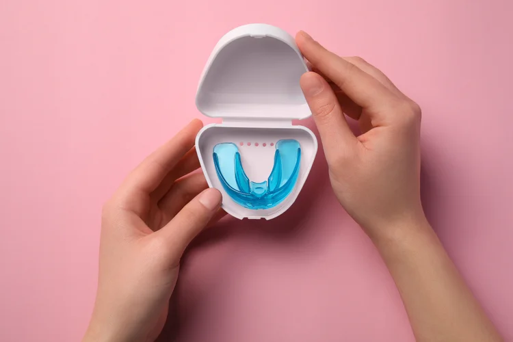Hands holding dental nightguard in case, used to prevent bruxism and protect teeth.