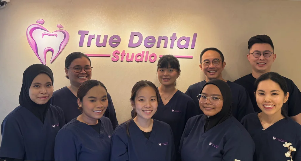 True Dental Studio’s friendly dental team standing in front of the clinic logo, smiling—representing one of the best dental clinics in Singapore.