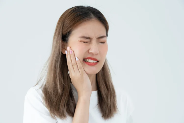 Young Asian woman holding cheek in pain showing possible wisdom tooth extraction complications.