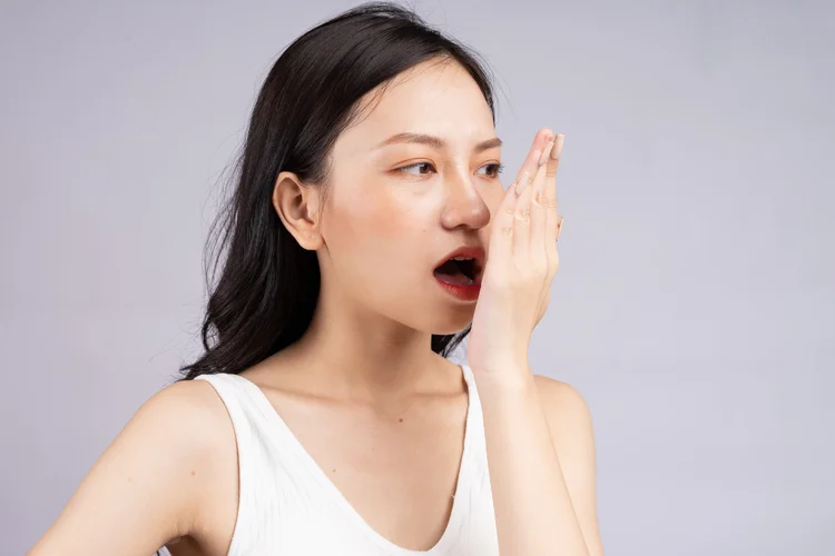Young woman covering mouth while checking breath, indicating oral freshness benefits after dental scaling.